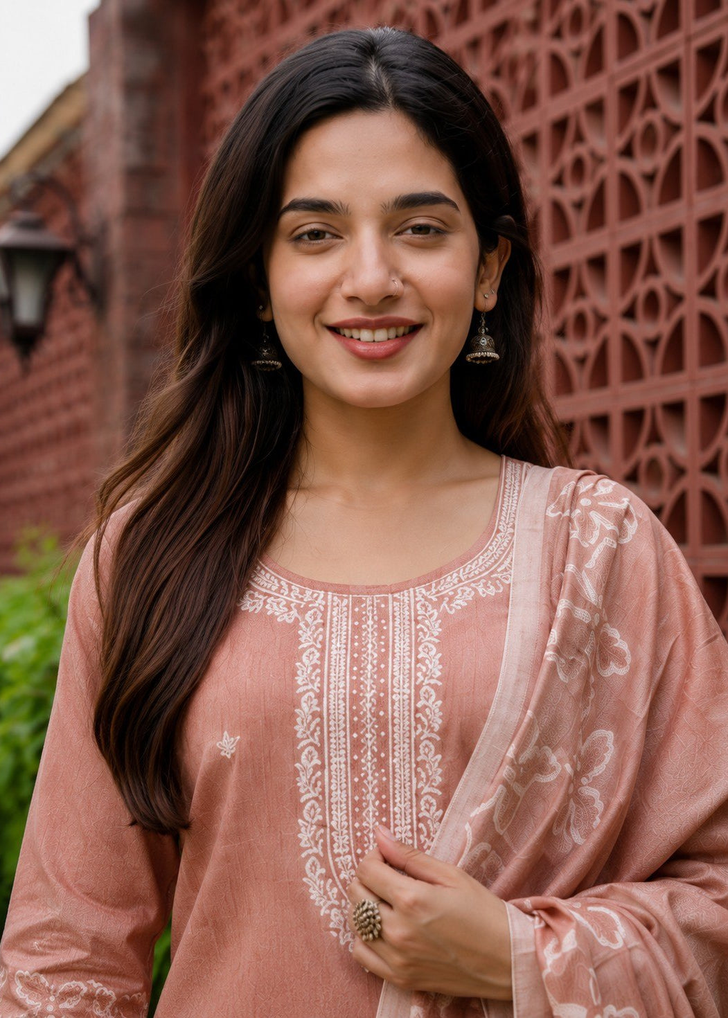 Woman wearing a pink embroidered traditional outfit in front of a decorative wall.