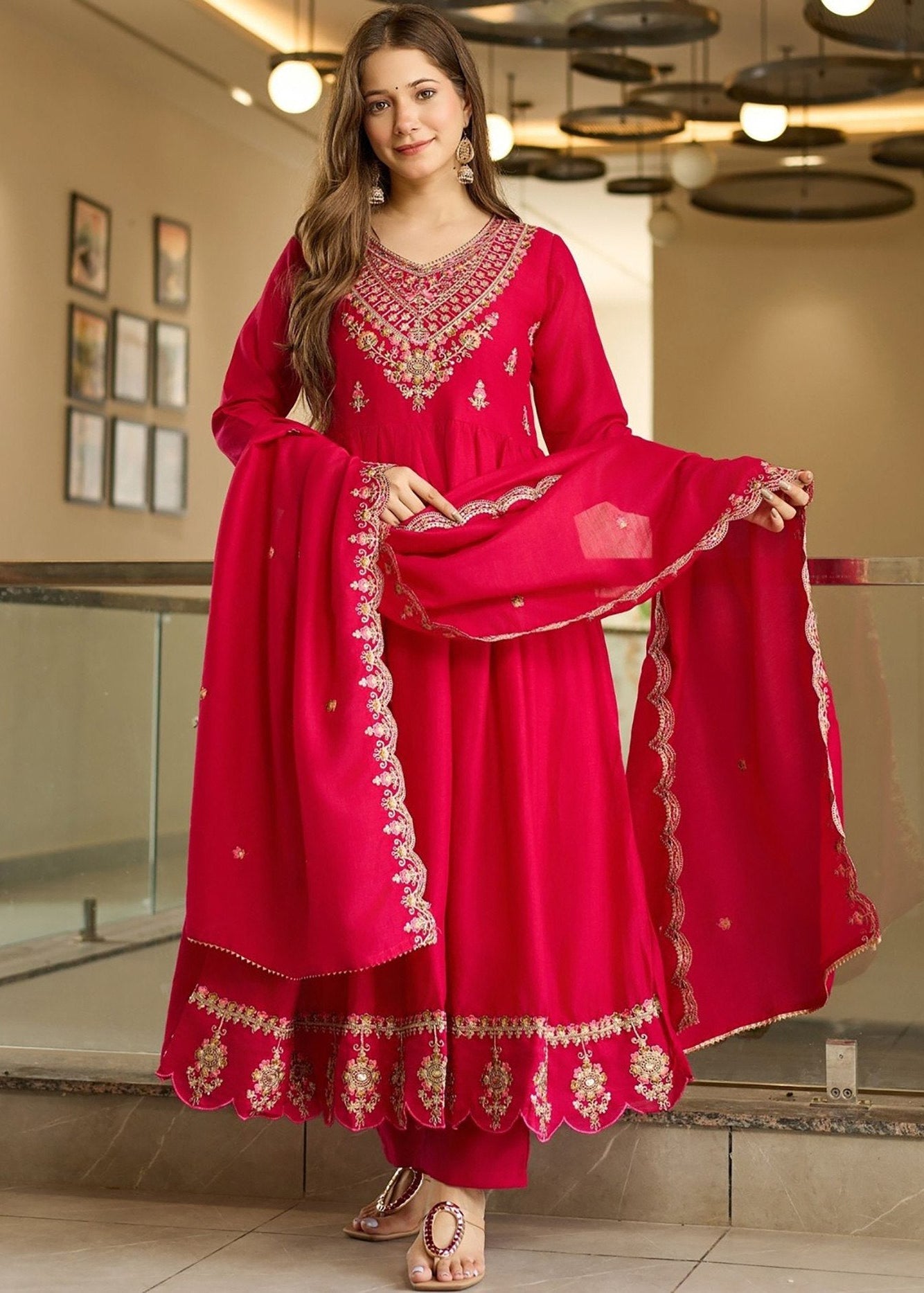 Woman wearing a bright pink traditional outfit with intricate embroidery indoors.
