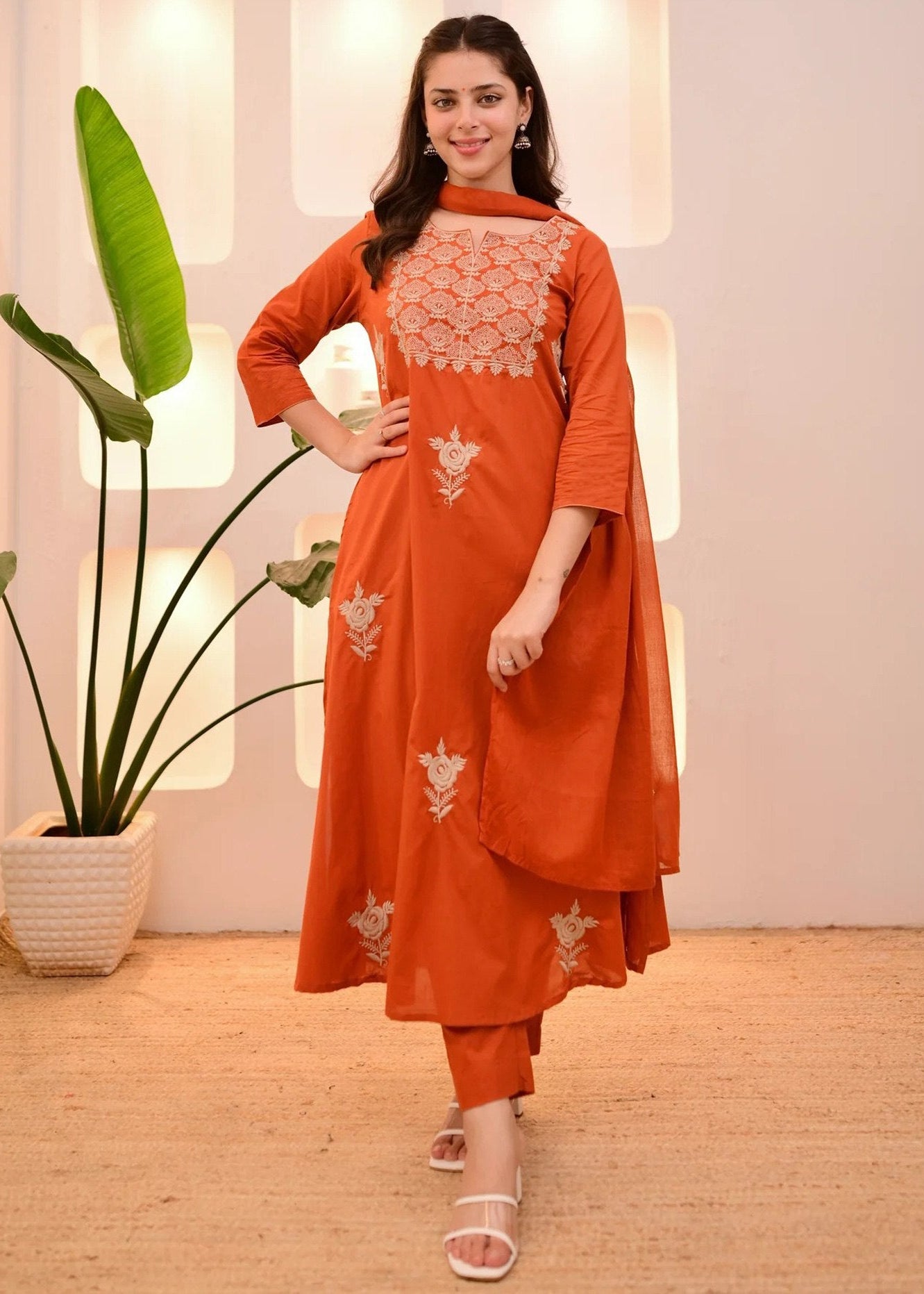 Woman wearing an orange traditional outfit with white embroidery in a bright room.