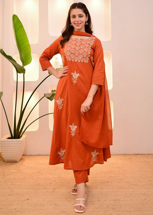 Woman wearing an orange traditional outfit with white embroidery in a bright room.