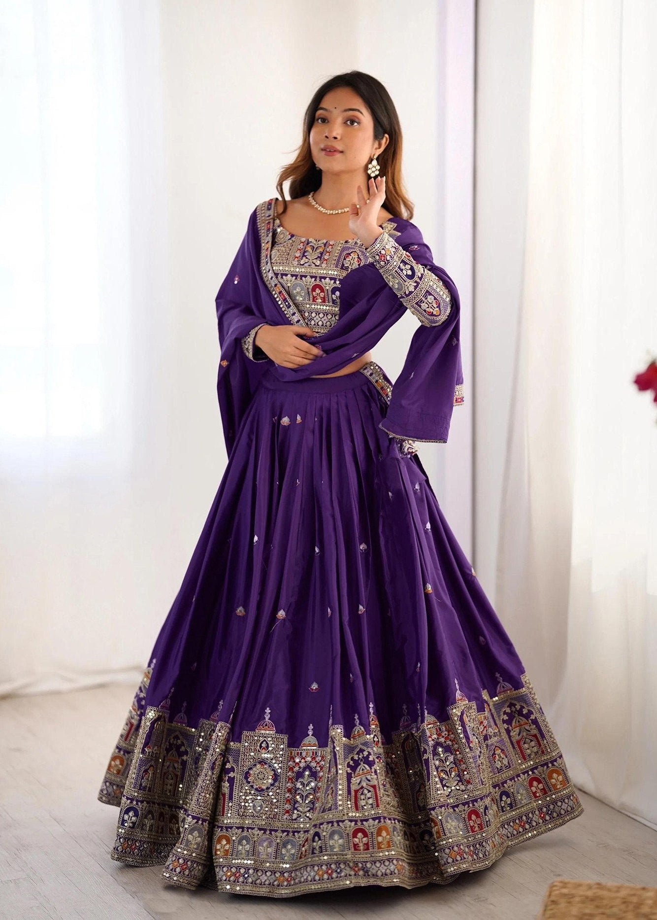 Woman wearing a purple embroidered traditional outfit against a white background