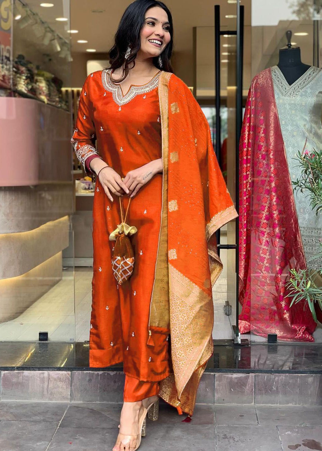 Woman in an orange traditional outfit standing in front of a store display.