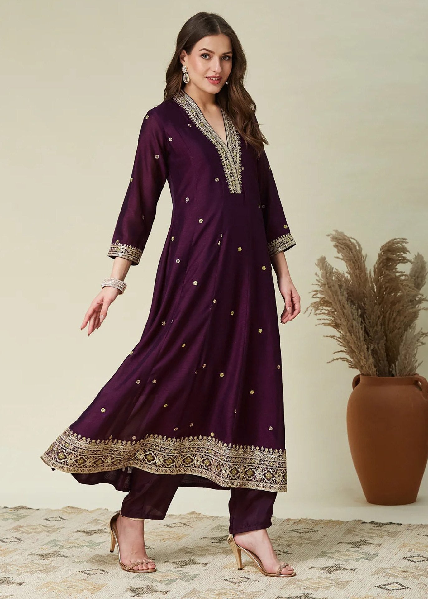 Woman wearing a purple traditional outfit with gold embroidery, standing against a neutral background.