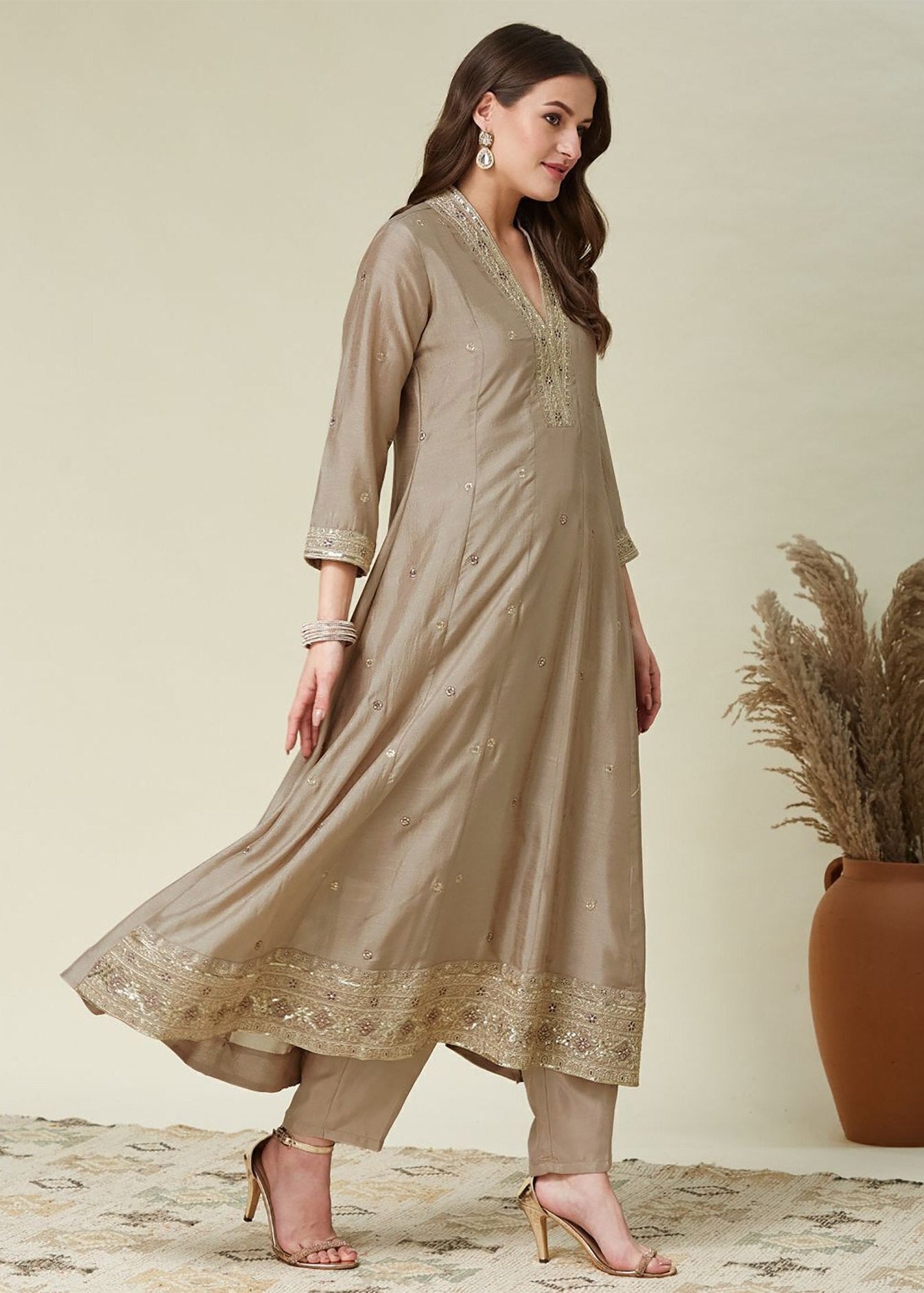 Woman wearing a beige kurta with lace details standing next to a vase with dried plants.