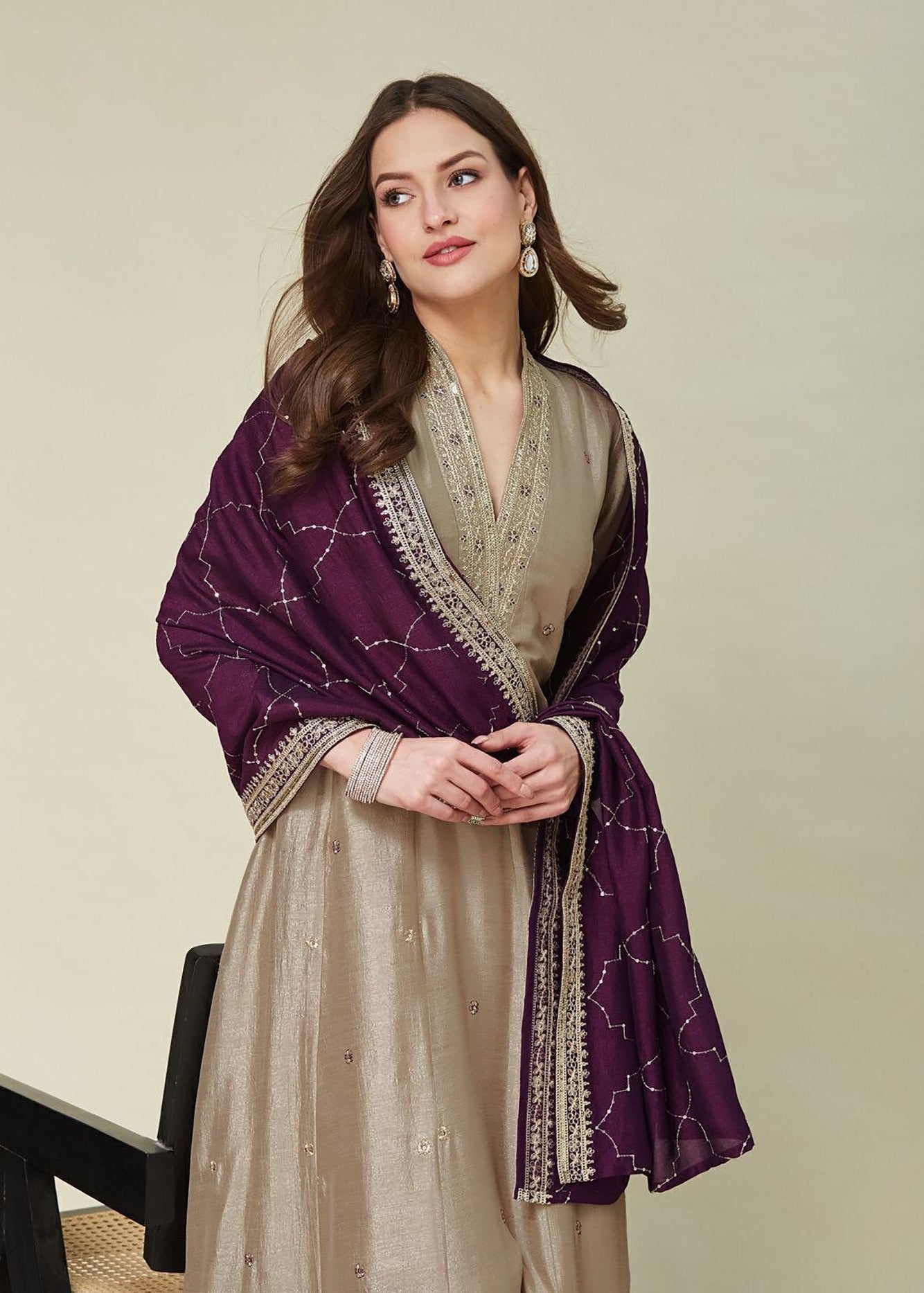 Woman wearing a beige outfit with a purple shawl on a light background