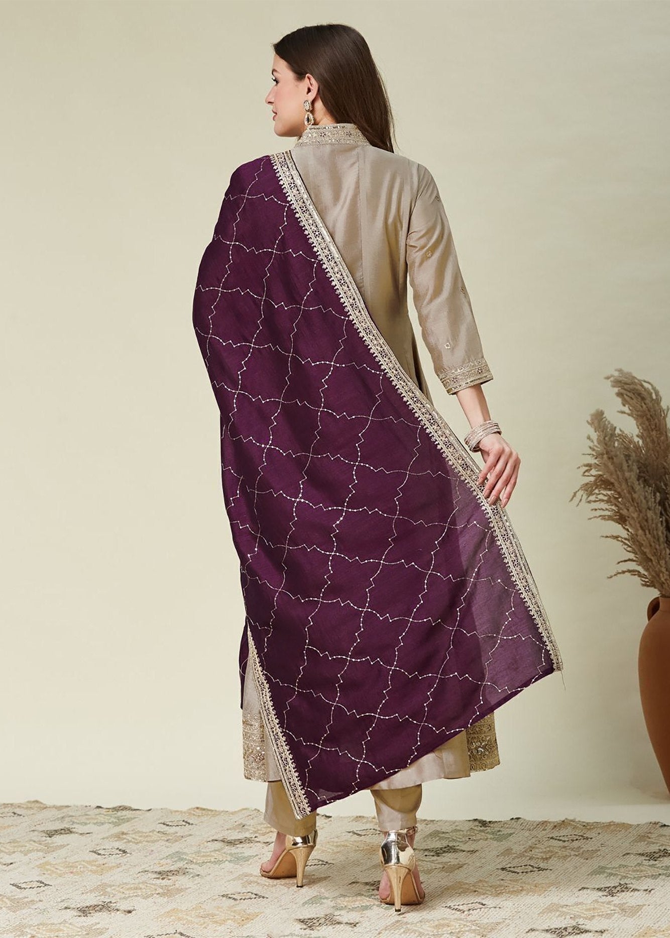 Woman wearing a beige kurta with a purple dupatta draped over her shoulder, standing against a plain background.