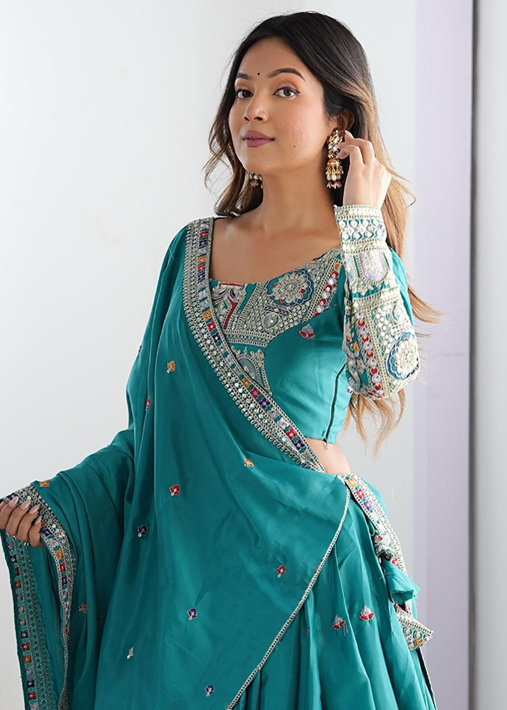 Woman wearing a teal saree with intricate embroidery against a white background