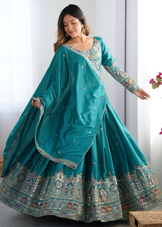 Woman wearing a teal traditional outfit with floral decorations indoors.