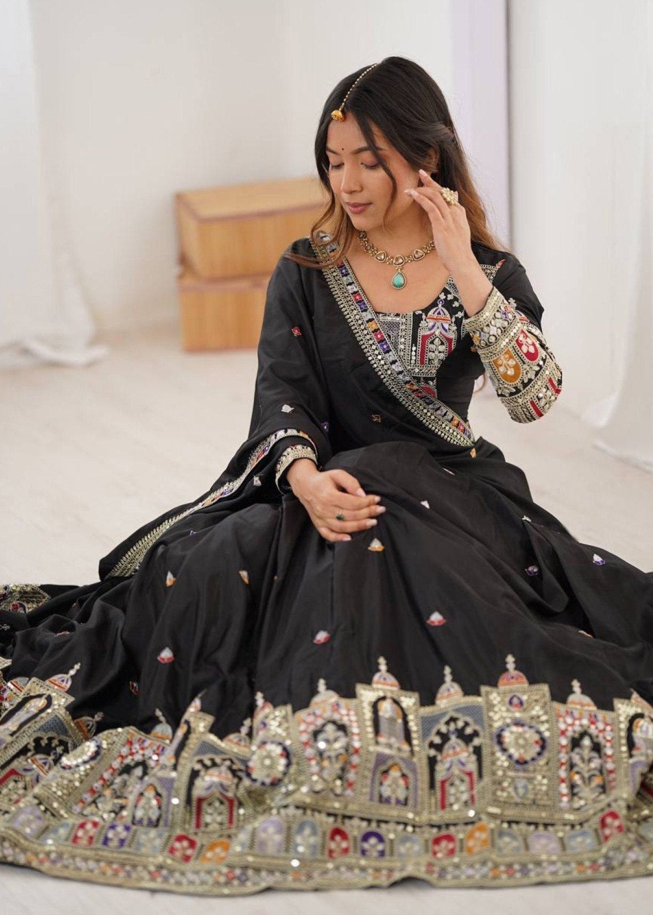 Woman in a black embroidered traditional outfit sitting on a white floor.