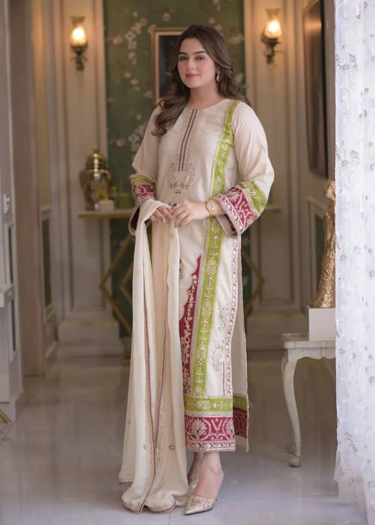 A woman wearing a cream Pure Roman Silk embroidered kurti set featuring maroon and green decorative embroidery, 3 mm sequence work, a matching stitched bottom, and a heavy embroidered faux georgette dupatta.