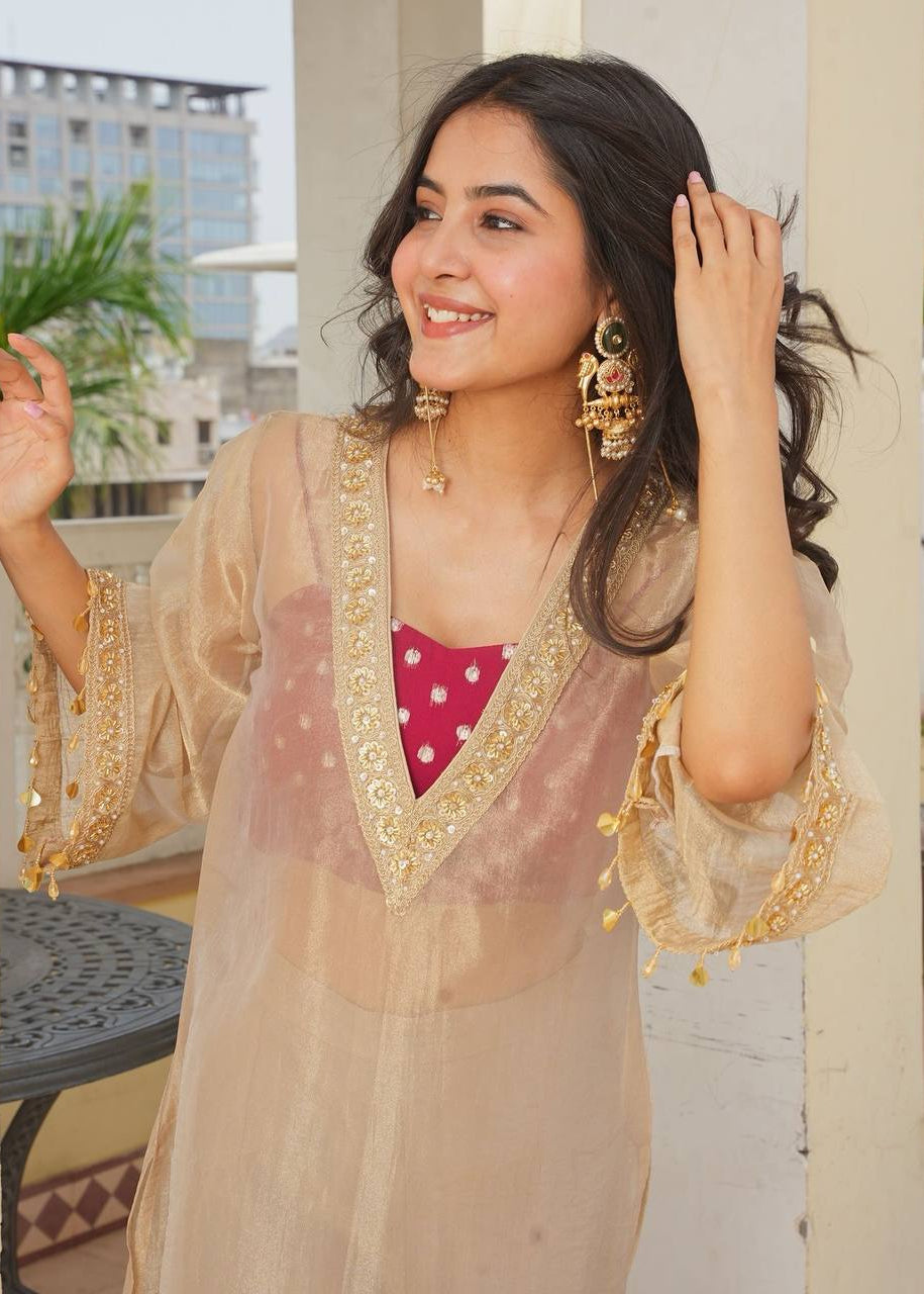 A woman wearing a beige sheer tissue febric embroidered kurta over a pink polka-dot brocade blouse with plazo