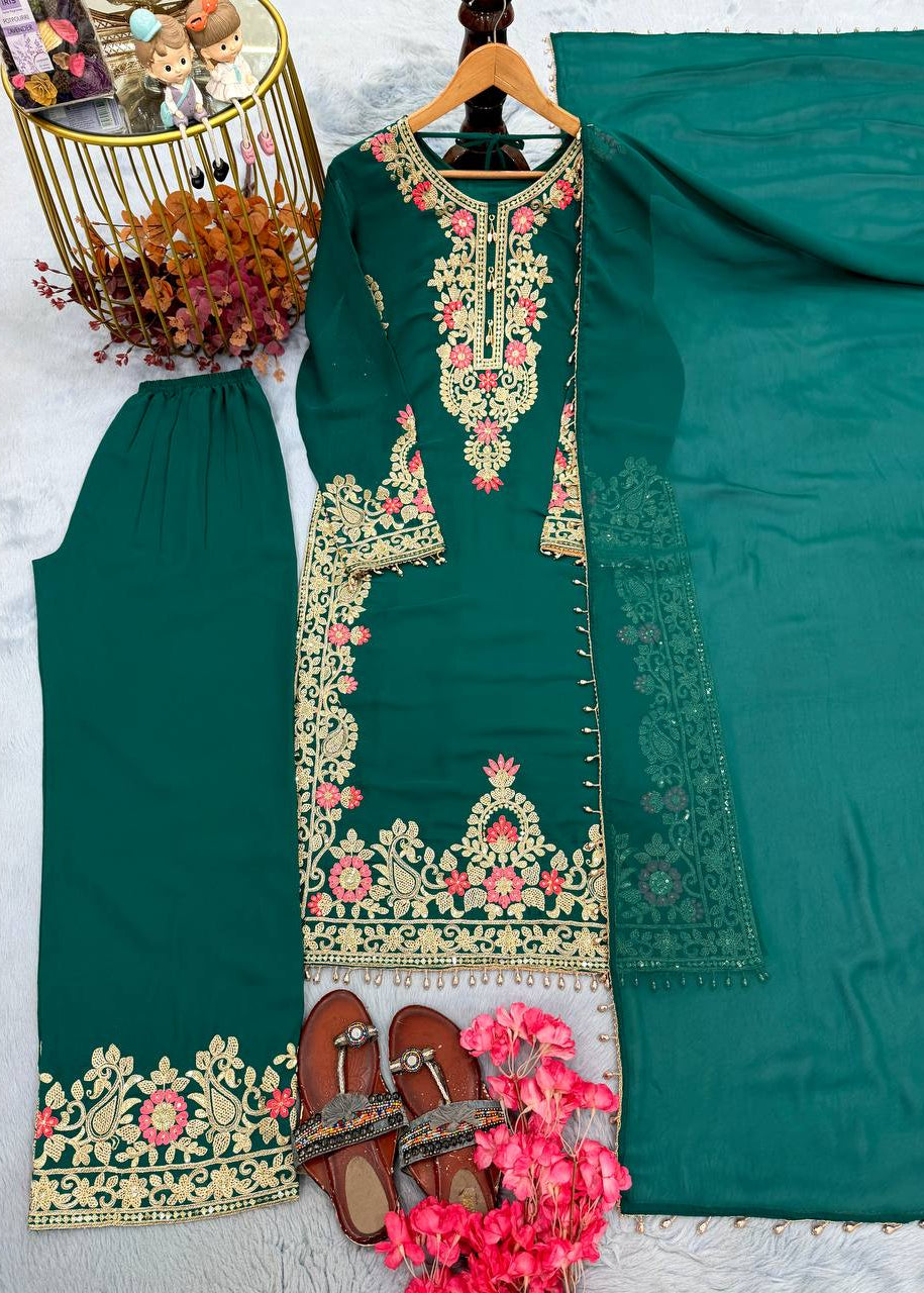 A dark teal green three-piece salwar kameez suit set with intricate gold, pink, and green floral embroidery, displayed on a hanger with matching trousers, a dupatta, and brown leather sandals on a white textured background.