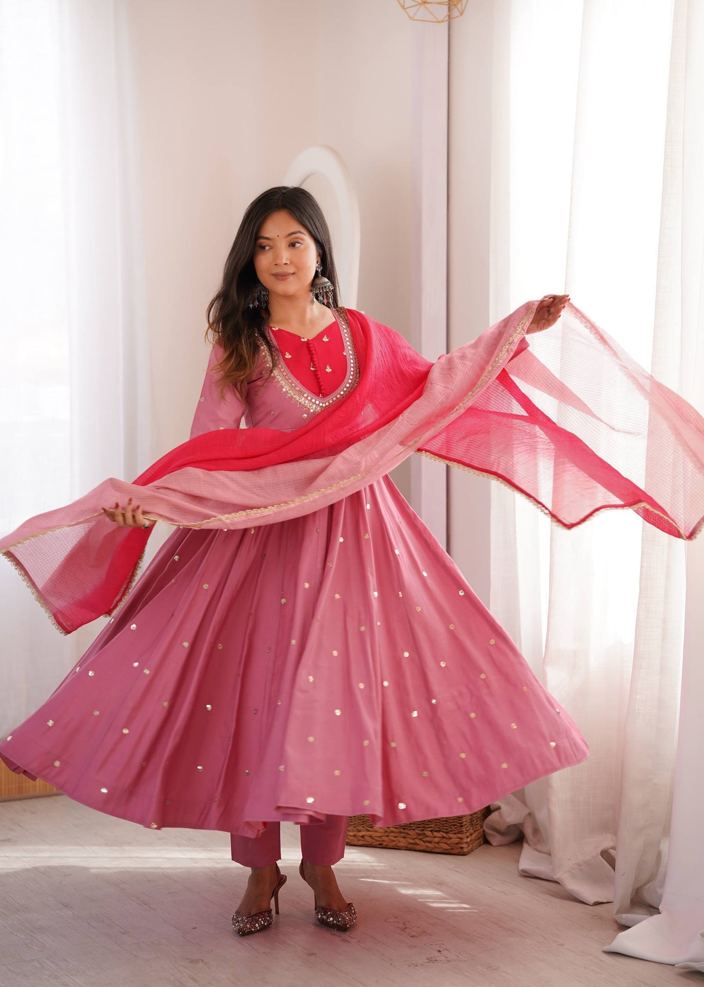 Woman in a pink traditional outfit with a red dupatta in a bright room.