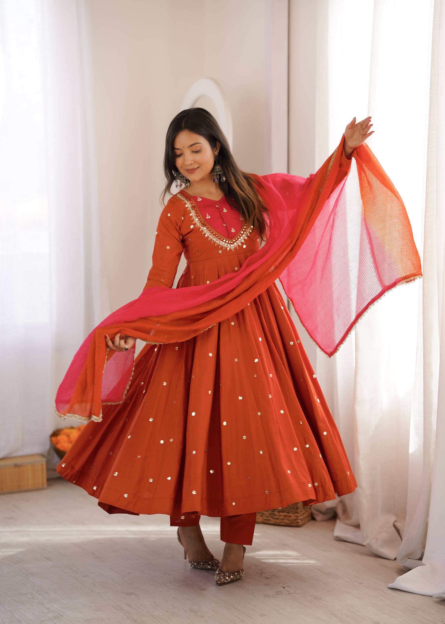 Woman in a traditional red and pink outfit with a matching dupatta, standing indoors.