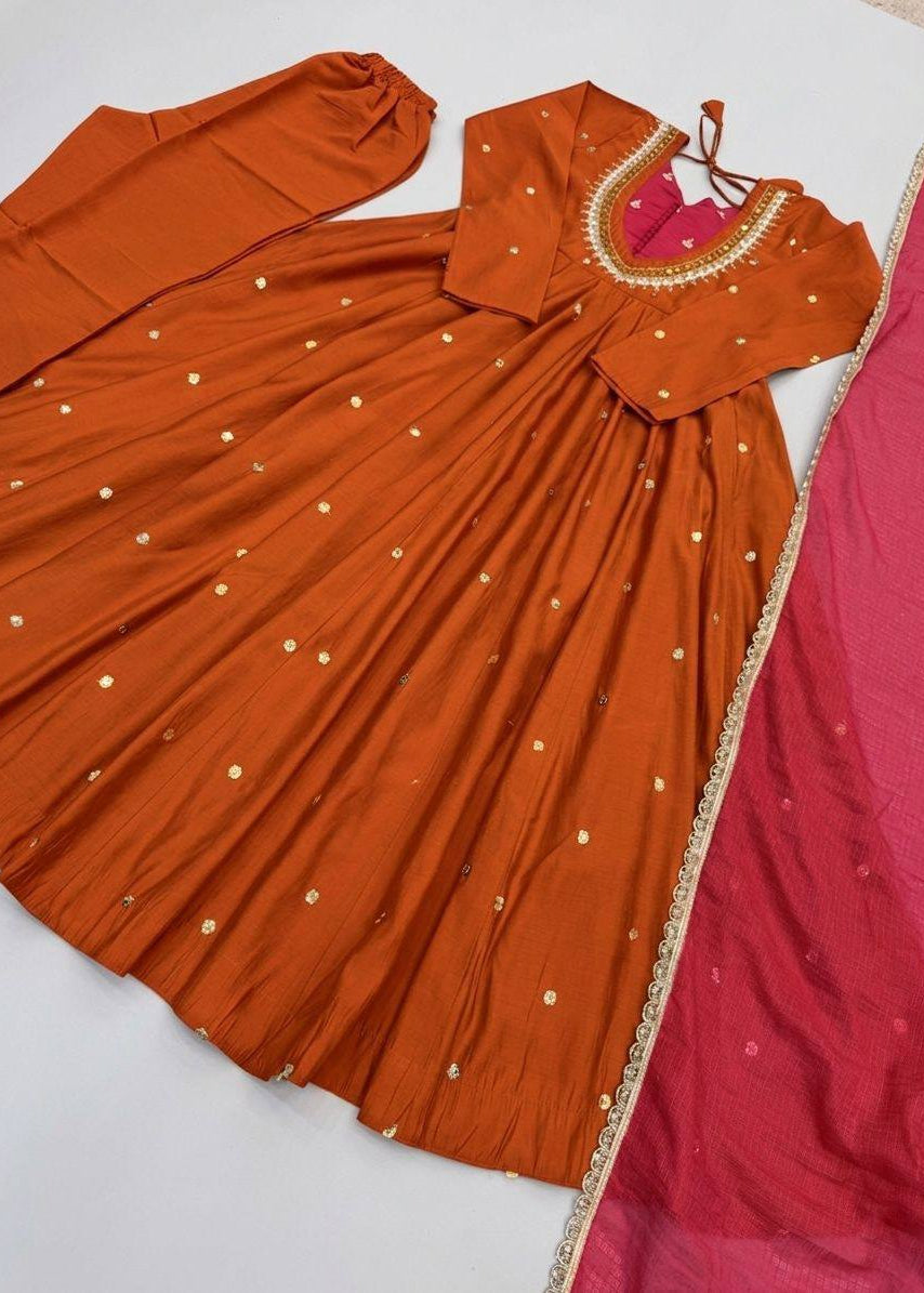 An orange traditional Anarkali gown with gold embroidered details and a matching pink dupatta with a gold border, laid flat on a white surface.