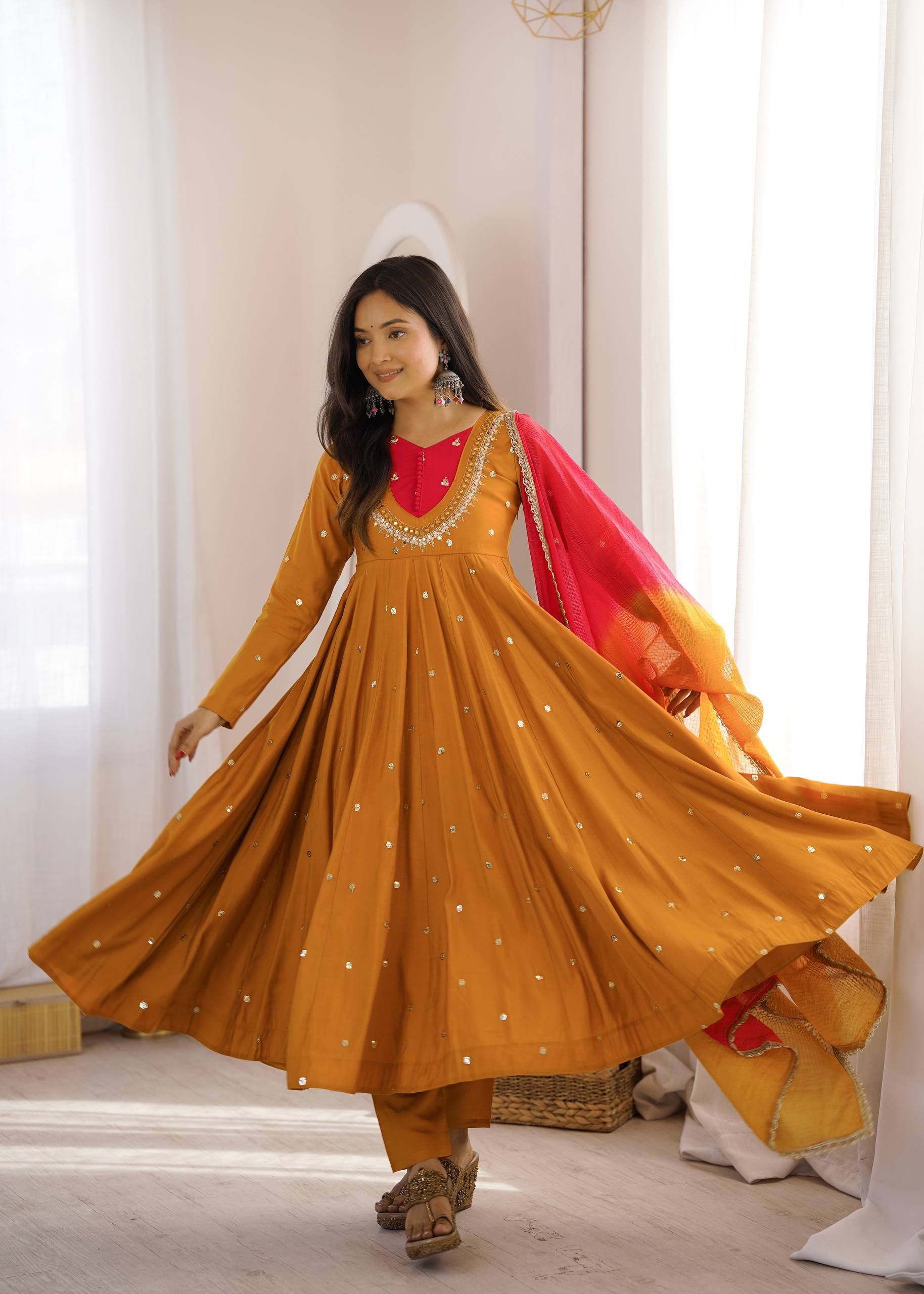 Woman in a mustard yellow traditional outfit with a red dupatta in a bright room.
