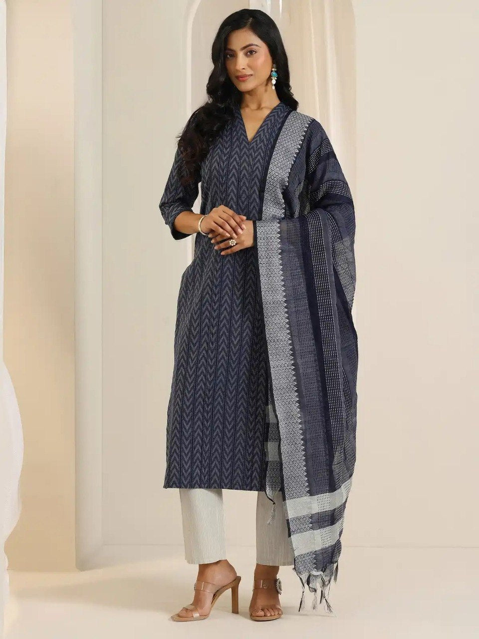 Woman wearing a navy blue kurta with white pants and a matching dupatta in a minimalistic setting.