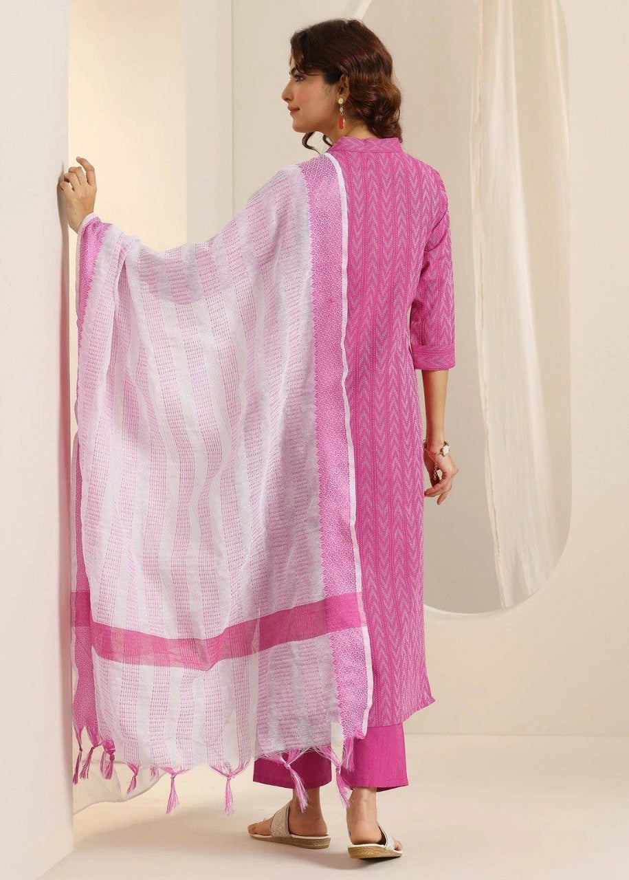 A woman wearing a bright pink kurta with a matching pink dupatta draped over her shoulder, shown from the back in a studio setting with a cream-colored background.